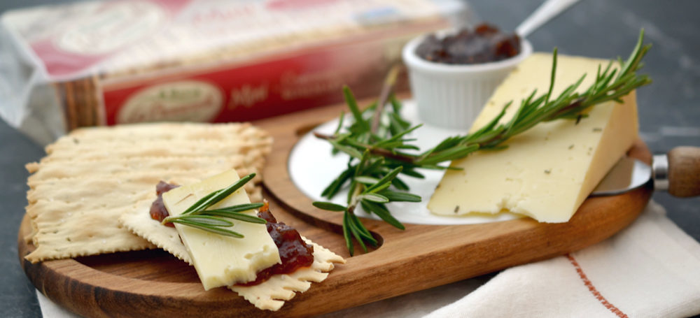 Rosemary Croccantini Cracker with jam, rosemary and cheese on a cutting board.