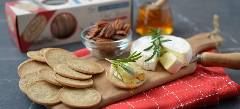 Rosemary Gluten Free Oat Thins on a cutting board with bre cheese and a sprig of rosemary